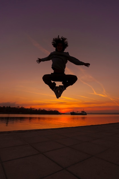Bezpłatne zdjęcie pełny strzał sylwetka człowieka skoki o zachodzie słońca