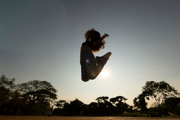 Bezpłatne zdjęcie pełny strzał sylwetka kobiety skoki o zachodzie słońca