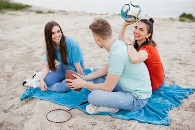 Pełny strzał szczęśliwi przyjaciele siedzi na plaży