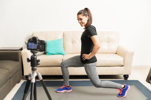 Pełny widok pięknej młodej kobiety pokazującej niektóre ćwiczenia na aparacie na jej vlog fitness