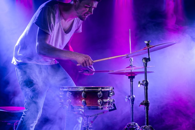 Perkusista gra na perkusji na niebiesko. piękne efekty specjalne światła i dymu. proces gry na instrumencie muzycznym.