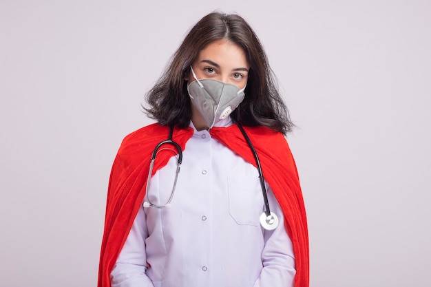 Pewna Młoda Kaukaska Dziewczyna Superbohatera W Czerwonej Pelerynie Ubrana W Mundur Lekarza I Stetoskop Z Maską Ochronną Odizolowaną Na Białej ścianie Z Kopią Przestrzeni