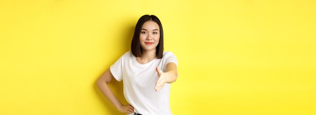 Pewna siebie azjatycka kobieta w białej koszulce wyciąga rękę do uścisku dłoni i gestu powitania, mówiąc hel