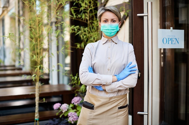 Pewna siebie kelnerka w masce ochronnej i rękawiczkach ponownie otwiera kawiarnię podczas epidemii koronawirusa