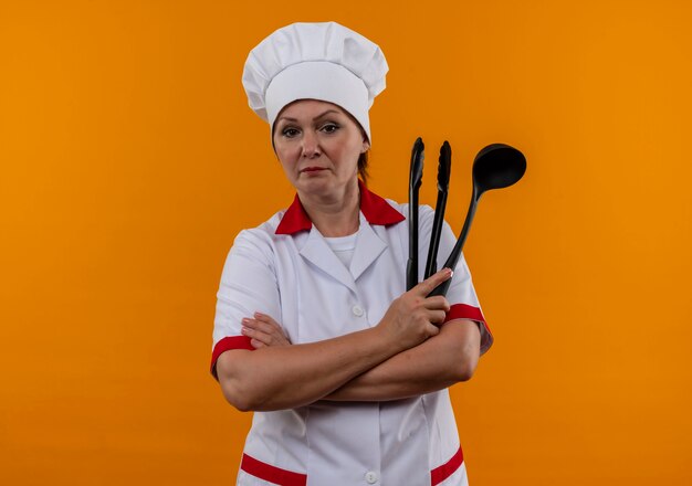 Pewna siebie w średnim wieku kucharka w mundurze szefa kuchni trzymając łopatkę na odosobnionej żółtej ścianie