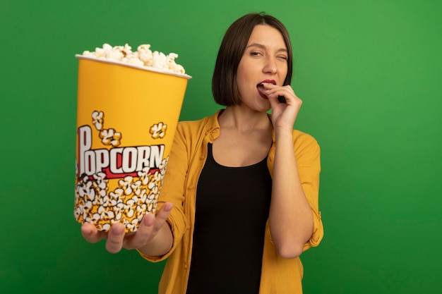 Pewnie Całkiem Kaukaska Kobieta Mruga Oczami, Jedząc I Trzymając Wiadro Popcornu Na Białym Tle