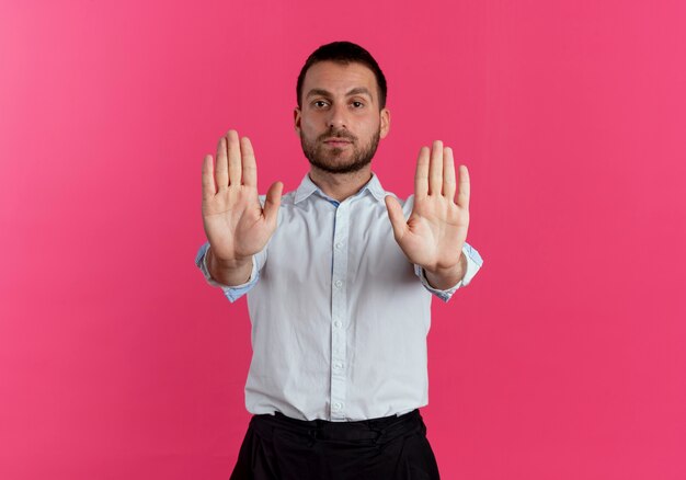 Pewnie przystojny mężczyzna gesty zatrzymują znak ręką dwiema rękami odizolowanymi na różowej ścianie