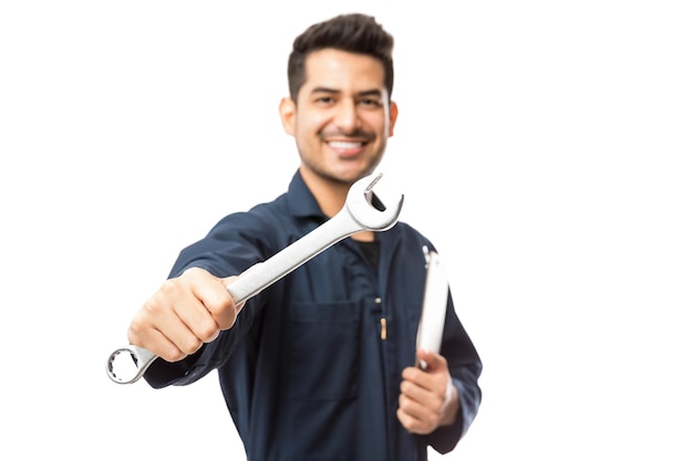 Pewny siebie i uśmiechnięty mężczyzna mechanik pokazujący klucz na białym tle