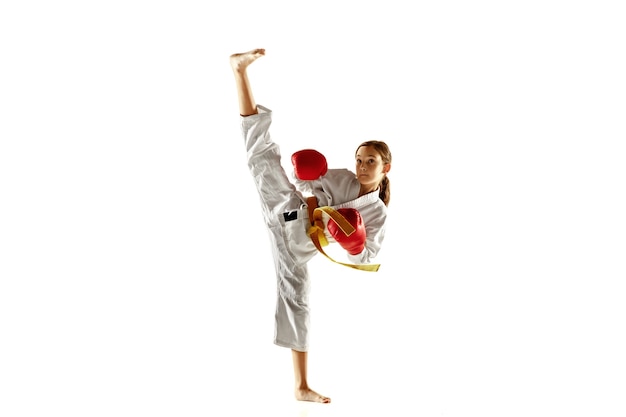Pewny siebie junior w kimonie ćwiczący walkę wręcz, sztuki walki. Młody żeński wojownik z żółtym pasem s trening na białej ścianie. Pojęcie zdrowego stylu życia, sportu, akcji.
