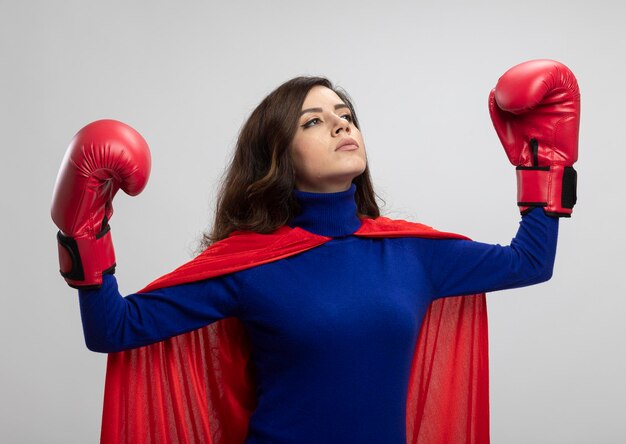 Pewny siebie superbohater kaukaski dziewczyna z czerwoną peleryną sobie na sobie rękawice bokserskie stoi z podniesioną