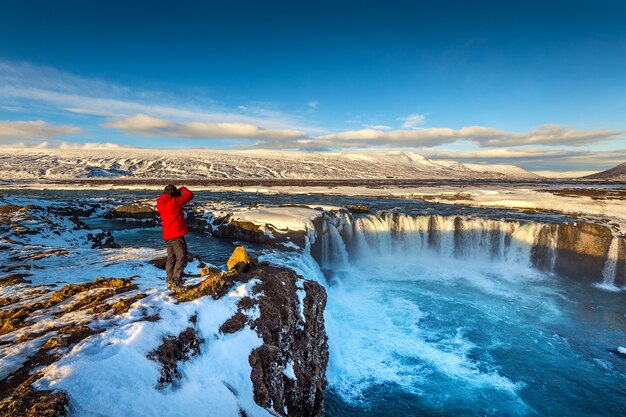 Photoghaper robi zdjęcie przy wodospadzie Godafoss zimą, Islandia.