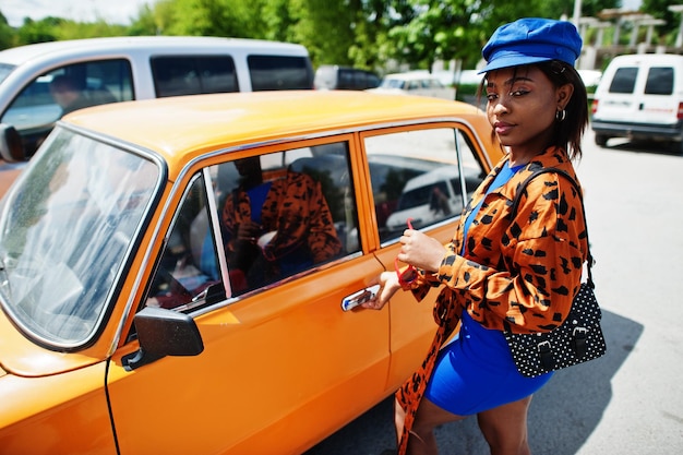 Piękna afroamerykańska dama w okularach przeciwsłonecznych stojąca w pobliżu pomarańczowego klasycznego samochodu retro