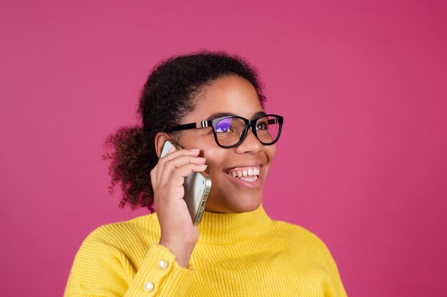 Piękna afroamerykańska kobieta na różowej ścianie rozmawia przez telefon komórkowy