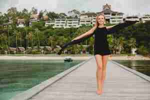 Bezpłatne zdjęcie piękna atrakcyjna kobieta ubrana w czarną sukienkę pozowanie na molo w luksusowym hotelu, wakacje, tropikalna plaża
