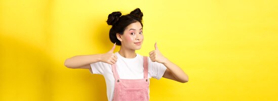 Bezpłatne zdjęcie piękna azjatycka dziewczyna z jasnoróżowym makijażem pokazująca kciuk w aprobacie i uśmiechająca się zadowolona reco