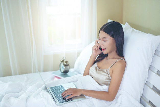 Piękna Azjatycka kobieta relaksuje się i pracuje z laptopem, czytając w domu.