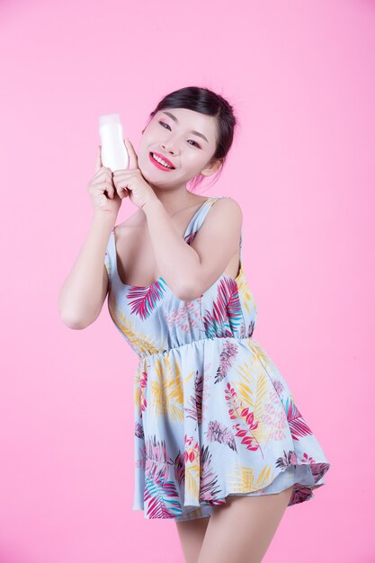Piękna Azjatycka kobieta trzyma butelkę produkt na różowym tle.