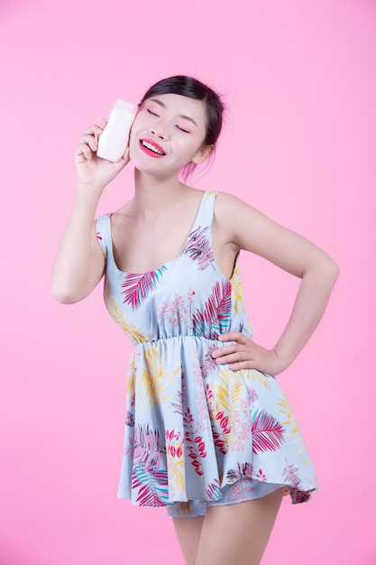 Piękna Azjatycka kobieta trzyma butelkę produkt na różowym tle.