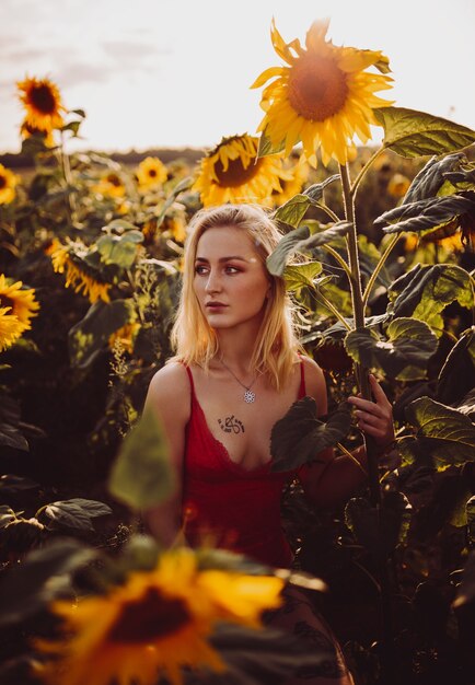 Piękna blondynka w czerwonej sukience w polu słoneczników