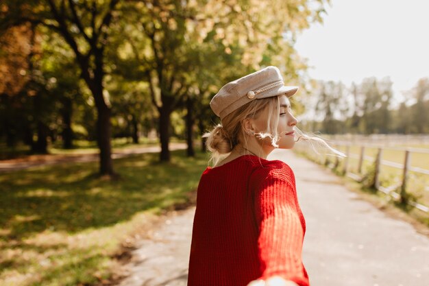 Piękna blondynka w modnych ciuchach prosi żartobliwie, żeby podążała za nią w parku. Ładna dziewczyna korzystających na zewnątrz słonecznej pogody.