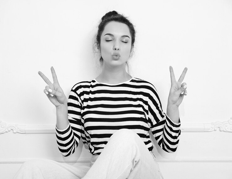 Bezpłatny plik Zdjęcie piękna brunetka kobieta dziewczyna model z nagim makijażu w letnie ubrania hipster pozowanie w pobliżu ściany. siedząc na podłodze, całując i pokazując znak pokoju