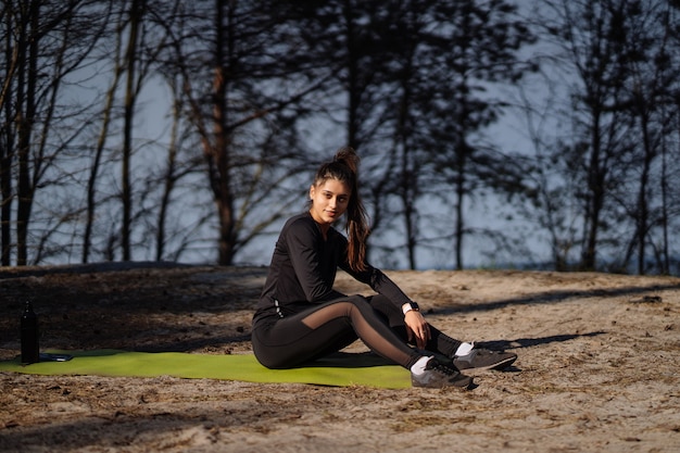 Piękna brunetka Kukaska ubrana w odzież sportową siedzi na macie w naturze