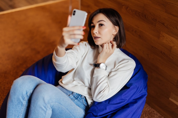 Piękna brunetka w niebieskich dżinsach i białym t-shircie sprawia, że selfie ma połączenie wideo na swoim telefonie