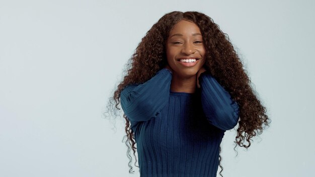 Piękna czarna afroamerykanka rasy mieszanej z długimi kręconymi włosami i idealnym uśmiechem, patrząc w kamerę i uśmiechając się na niebiesko