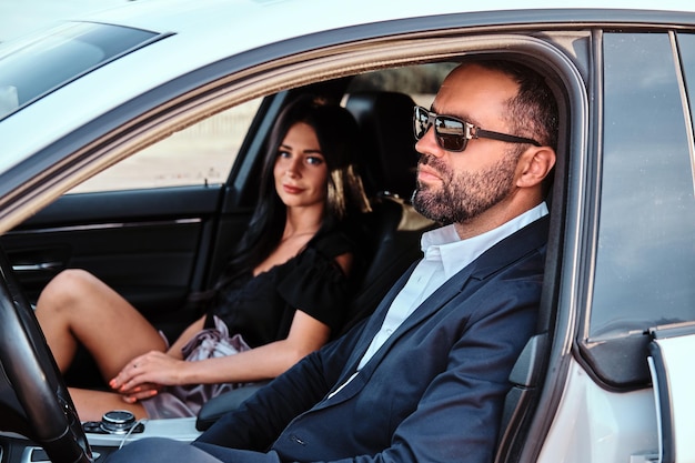 Piękna, dobrze ubrana para siedzi na przednich siedzeniach w luksusowym samochodzie.