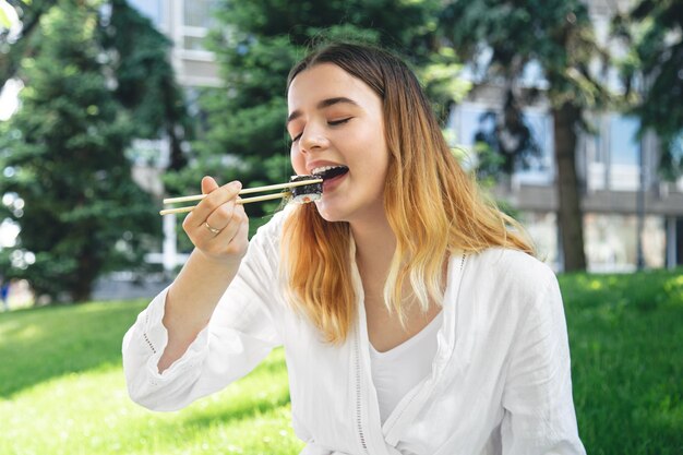 Piękna dziewczyna je sushi siedząc na trawie w parku