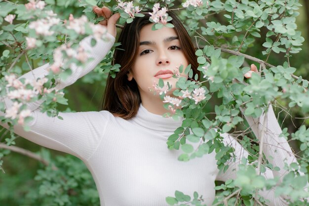 Piękna dziewczyna ma sesję zdjęciową w kwitnącym parku, trzymając gałąź w kwiecie
