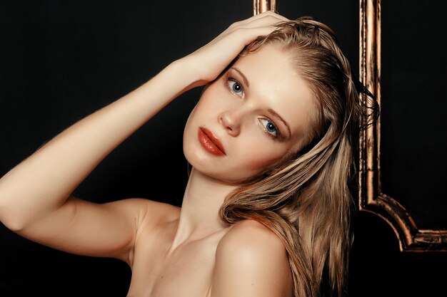 Piękna dziewczyna moda model naturalny makijaż mokre włosy na czarnym tle złota w ciepłych kolorach. portret młodej kobiety z makijażem mody