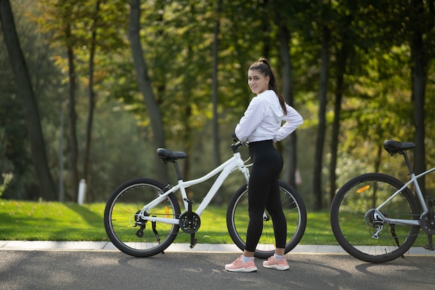 Piękna dziewczyna pozuje na białym rowerze. Spaceruj na łonie natury.