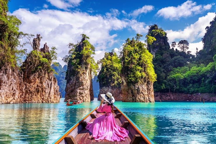 Bezpłatny plik Zdjęcie piękna dziewczyna siedzi na łodzi i patrząc na góry w ratchaprapha dam w parku narodowym khao sok, prowincja surat thani, tajlandia.