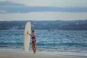 Bezpłatne zdjęcie piękna dziewczyna stoi na plaży z deską surfingową.