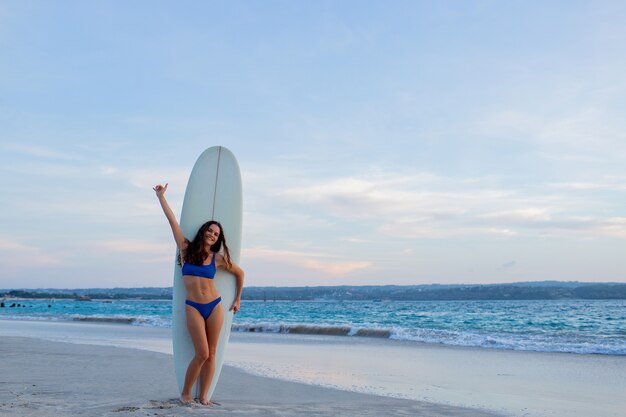 Piękna dziewczyna stoi na plaży z deską surfingową.