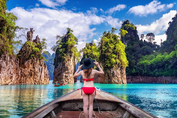 Bezpłatny plik Zdjęcie piękna dziewczyna stojąc na łodzi i patrząc na góry w ratchaprapha dam w parku narodowym khao sok, prowincja surat thani, tajlandia.