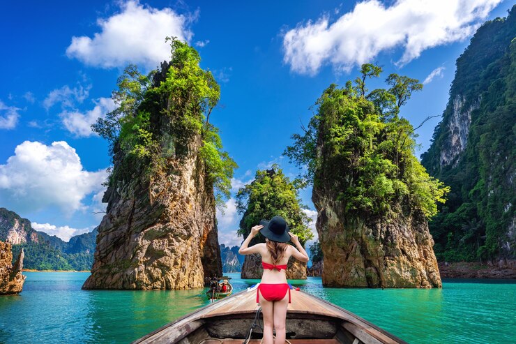 Bezpłatny plik Zdjęcie piękna dziewczyna stojąc na łodzi i patrząc na góry w ratchaprapha dam w parku narodowym khao sok, prowincja surat thani, tajlandia.