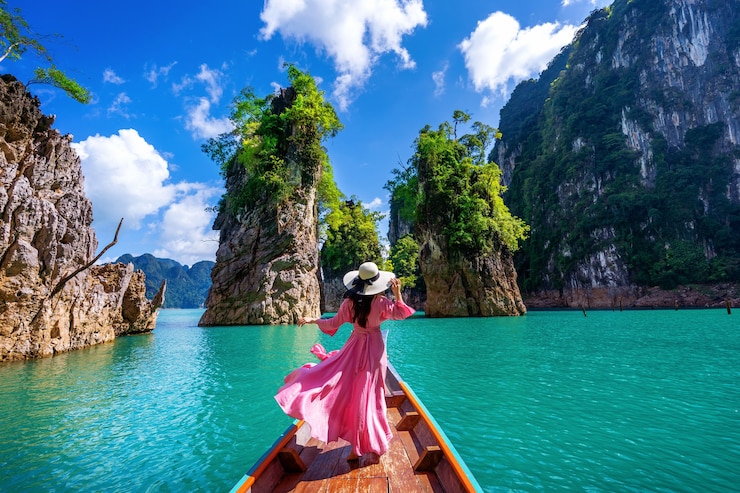 Bezpłatny plik Zdjęcie piękna dziewczyna stojąc na łodzi i patrząc na góry w ratchaprapha dam w parku narodowym khao sok, prowincja surat thani, tajlandia.