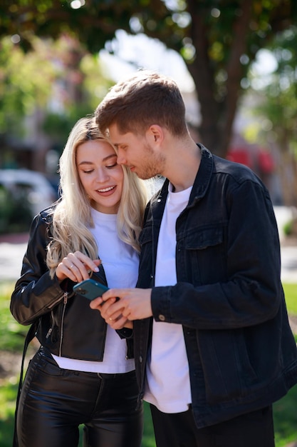 Bezpłatne zdjęcie piękna dziewczyna uśmiecha się i patrzy na telefon swojego chłopaka