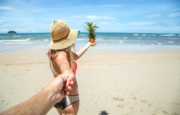 Piękna Dziewczyna W Stroju Kąpielowym I Ananasie Spacery Po Plaży, Trzymając Rękę Faceta