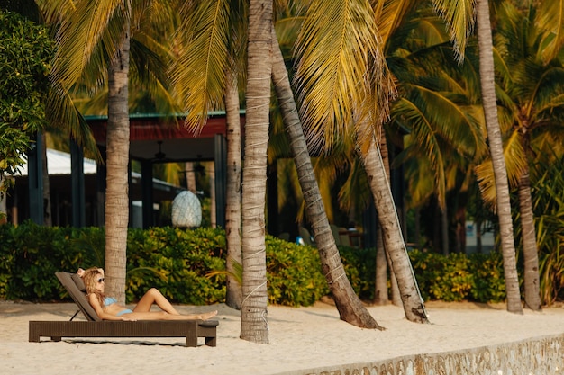 Bezpłatne zdjęcie piękna dziewczyna w stroju kąpielowym leżąca na leżaku pod palmami