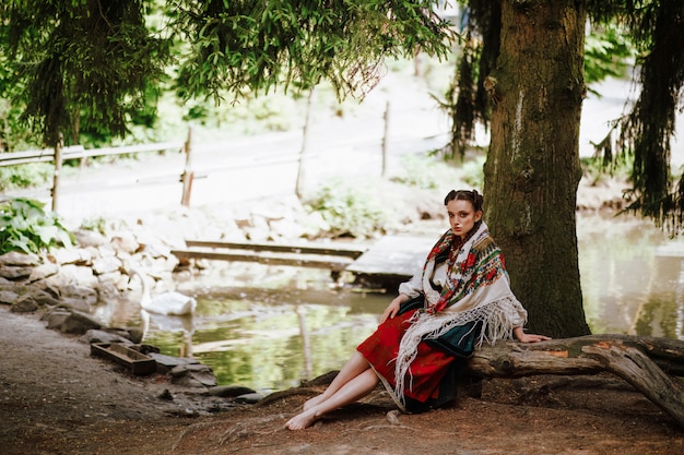 Piękna dziewczyna w ukraińskiej haftowanej sukni siedzi na ławce w pobliżu jeziora