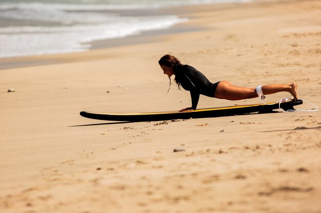 Piękna dziewczyna wstaje na desce surfingowej na piasku.