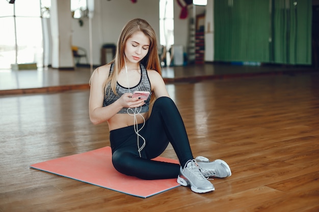 Piękna i sportowa dziewczyna sportowa siedzi w sali gimnastycznej z telefonu
