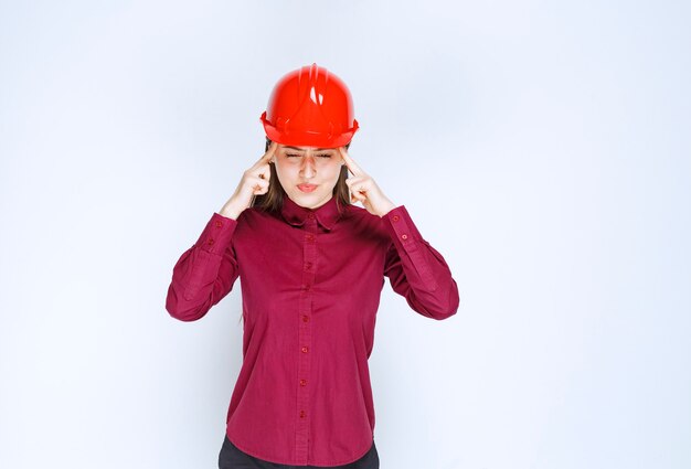Piękna kobieta architekt w czerwonym kasku stoi i ciężko myśli.