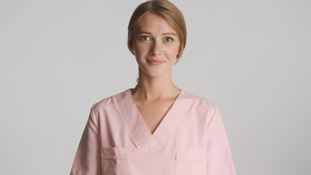 Piękna kobieta blond lekarz w mundurze pozuje na aparacie na białym tle