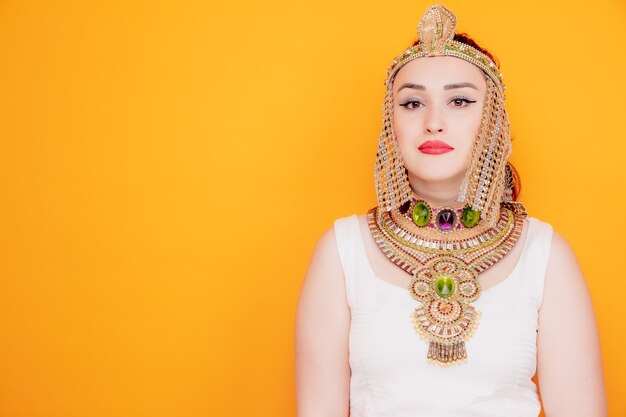 Piękna kobieta jak Kleopatra w starożytnym egipskim stroju z poważnym, pewnym siebie wyrazem na pomarańczowo