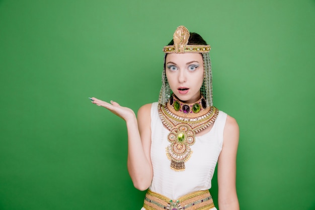 Piękna Kobieta Jak Kleopatra W Starożytnym Egipskim Stroju Zdumiona I Zdziwiona, Prezentując Coś Ramieniem Dłoni Na Zielono