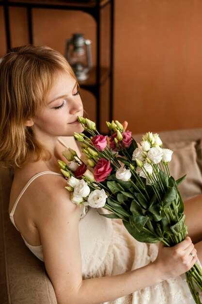 Piękna kobieta pozuje na kanapie, trzymając bukiet wiosennych kwiatów
